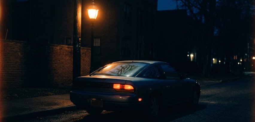Streetlamp isolates a car's rear window and taillight at night Rear of a classic coupe under a single streetlamp, one taillight glowing in the light.